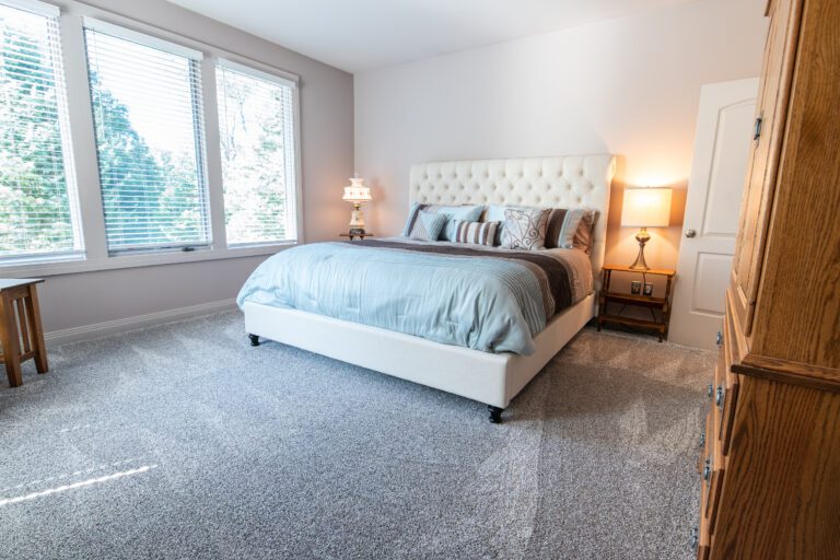 Main bedroom with newly cleaned carpets, vacuum lines on gray carpet, made bed