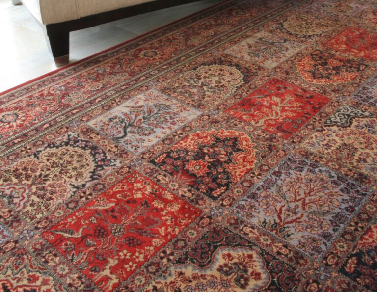 Close up of oriental rug with several patterns, upholstered chair in the background