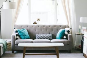 Grey upholstered couch in front of the living room window with a white and brown cat sitting on it