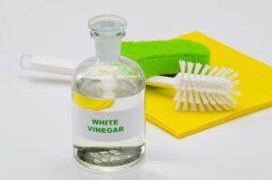 White vinegar in a glass bottle, cleaning scrubber and cloth in the background