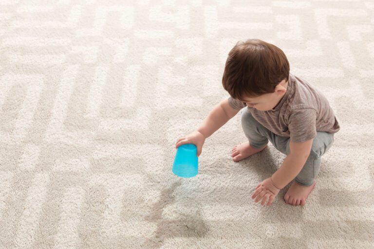 Little boy spilling a cup of water onto the carpet